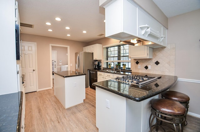 kitchen with a peninsula, a kitchen island, a kitchen bar, and white cabinetry