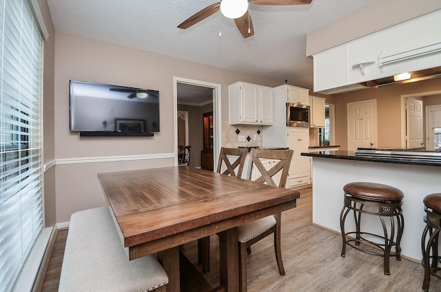 dining space featuring light wood-type flooring, a healthy amount of sunlight, a ceiling fan, and a textured ceiling