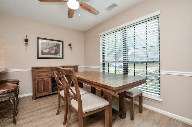 dining room featuring light wood-type flooring, ceiling fan, visible vents, and baseboards