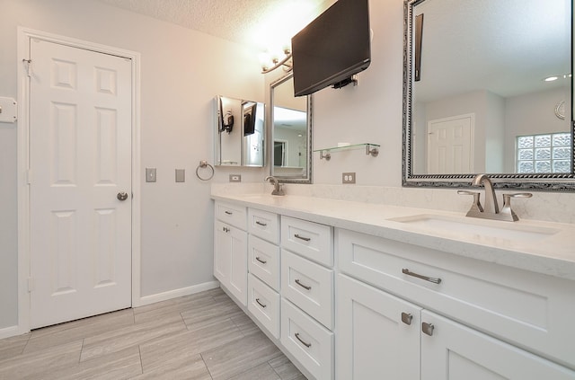 full bath featuring double vanity, a textured ceiling, baseboards, and a sink