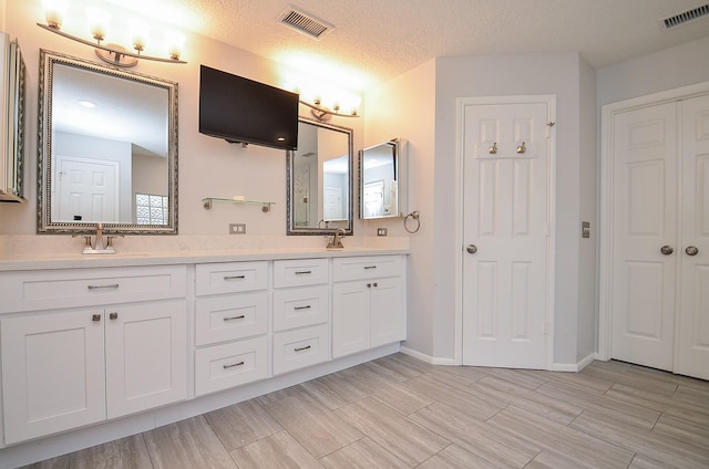 full bathroom with visible vents, a sink, a textured ceiling, and double vanity