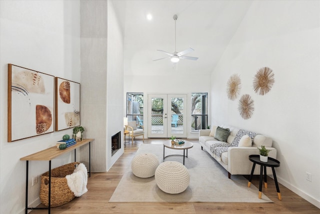 living area featuring french doors, light wood-style flooring, ceiling fan, high vaulted ceiling, and baseboards