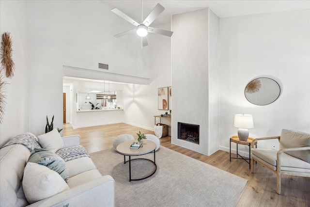 living area with visible vents, light wood-style flooring, a towering ceiling, a large fireplace, and ceiling fan