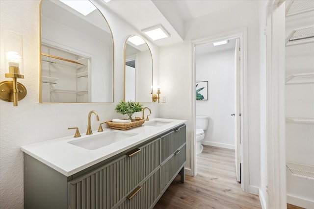 bathroom with a spacious closet, wood finished floors, a sink, and toilet