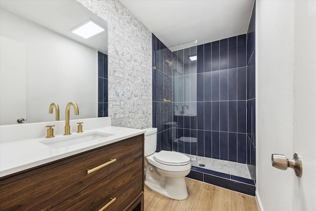 bathroom featuring a tile shower, vanity, toilet, and wood finished floors