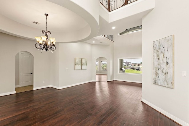 unfurnished living room featuring visible vents, arched walkways, dark wood finished floors, baseboards, and a towering ceiling