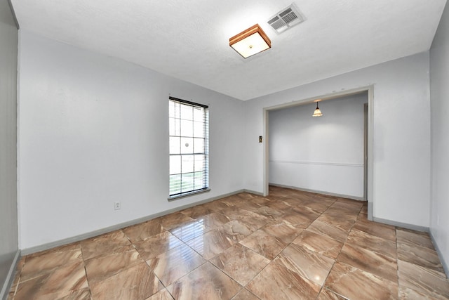 empty room featuring visible vents, a textured ceiling, and baseboards