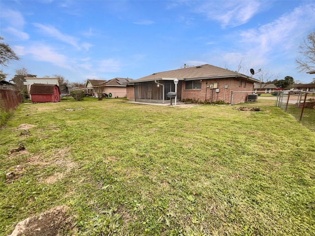 view of yard with a sunroom, a fenced backyard, an outbuilding, and a shed