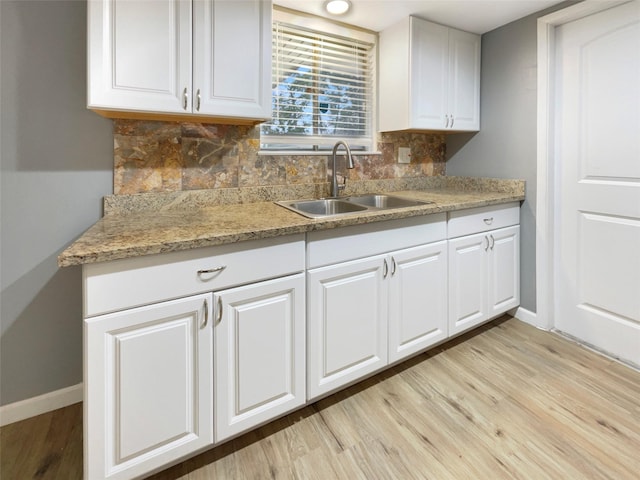 kitchen with light wood-type flooring, decorative backsplash, white cabinets, and a sink