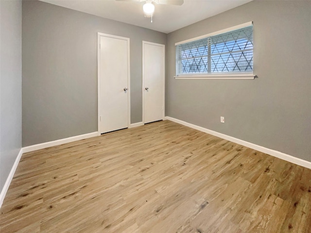 unfurnished bedroom with light wood-style floors, a ceiling fan, baseboards, and two closets