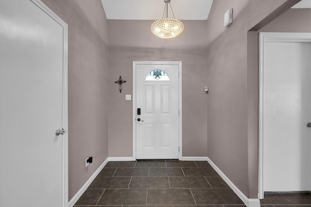 foyer featuring baseboards, a chandelier, and dark tile patterned flooring