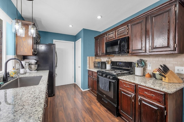 kitchen with light stone counters, a sink, black appliances, tasteful backsplash, and dark wood finished floors