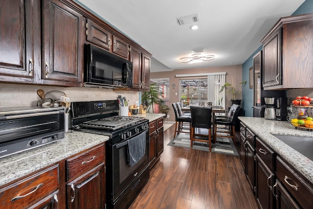 kitchen with dark brown cabinetry, dark wood-style flooring, visible vents, backsplash, and black appliances