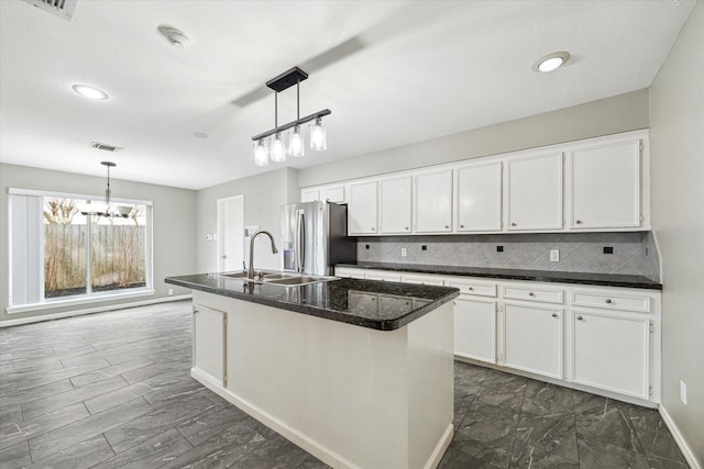 kitchen featuring stainless steel fridge, a center island with sink, white cabinetry, pendant lighting, and a sink