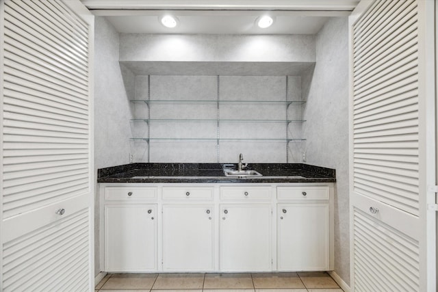 kitchen with light tile patterned floors, dark stone countertops, a sink, and white cabinets