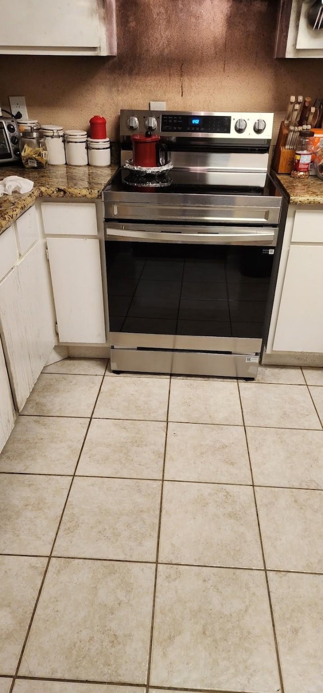 kitchen featuring light tile patterned floors, electric stove, stone counters, and white cabinets