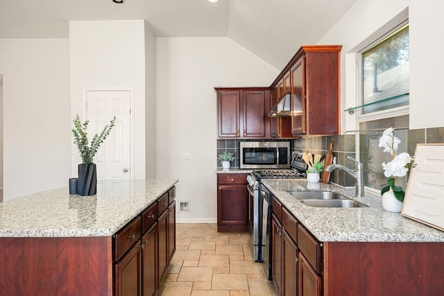 kitchen featuring under cabinet range hood, stainless steel appliances, a sink, stone finish flooring, and tasteful backsplash