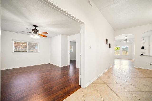 interior space featuring a textured ceiling, arched walkways, a ceiling fan, and light tile patterned flooring