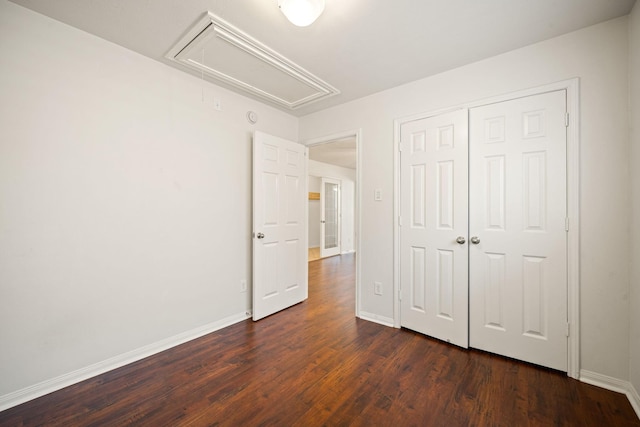 unfurnished bedroom with dark wood-style flooring, a closet, attic access, and baseboards