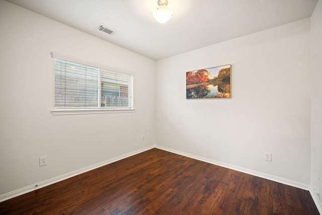 unfurnished room featuring dark wood-style floors, visible vents, and baseboards