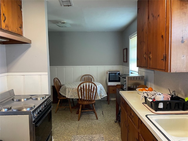 kitchen featuring a wainscoted wall, visible vents, light countertops, brown cabinetry, and range with electric cooktop