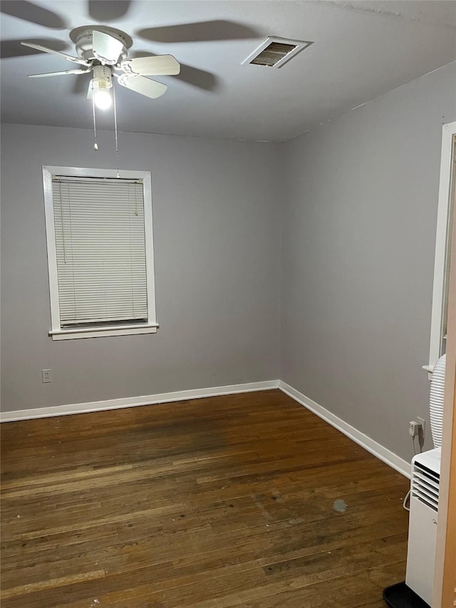 empty room featuring ceiling fan, dark wood finished floors, visible vents, and baseboards