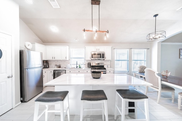 kitchen with pendant lighting, stainless steel appliances, a kitchen island, and white cabinets