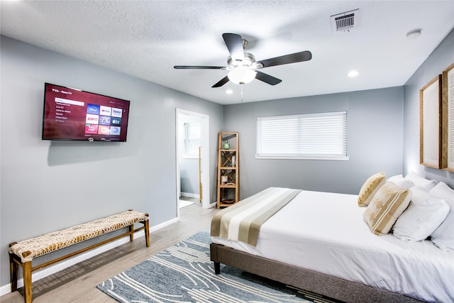 bedroom with a textured ceiling, light wood-style flooring, a ceiling fan, visible vents, and baseboards