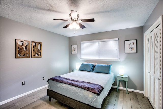 bedroom with baseboards, a ceiling fan, wood finished floors, a textured ceiling, and a closet