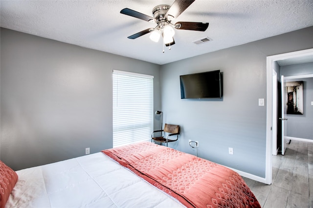 bedroom with a textured ceiling, visible vents, baseboards, light wood-style floors, and multiple windows