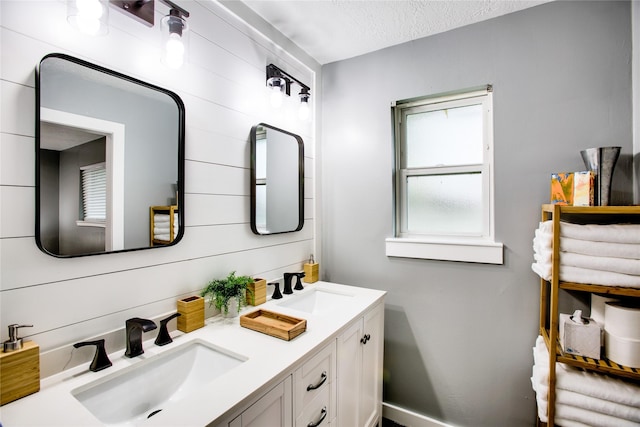 full bath featuring a textured ceiling, double vanity, and a sink