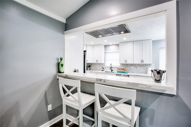 kitchen featuring a sink, white cabinets, light countertops, backsplash, and a kitchen bar