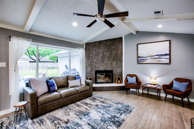 living room featuring a textured ceiling, a premium fireplace, lofted ceiling with beams, and light wood-style floors