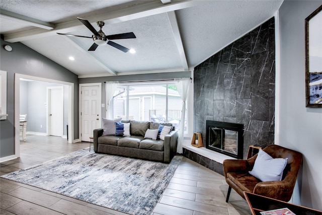 living area featuring light wood finished floors, lofted ceiling with beams, a tiled fireplace, ceiling fan, and a textured ceiling