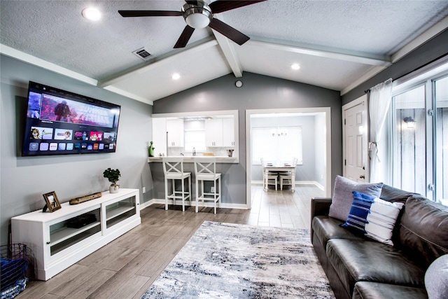 living area with a textured ceiling, lofted ceiling with beams, wood finished floors, visible vents, and baseboards