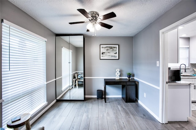 office featuring a sink, light wood-style floors, baseboards, and a textured ceiling