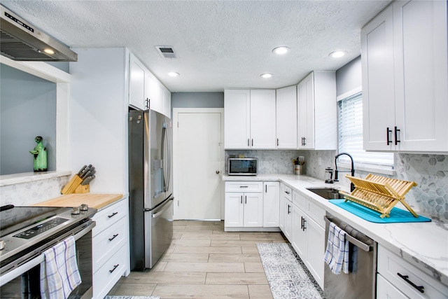 kitchen with stainless steel appliances, visible vents, white cabinetry, a sink, and extractor fan