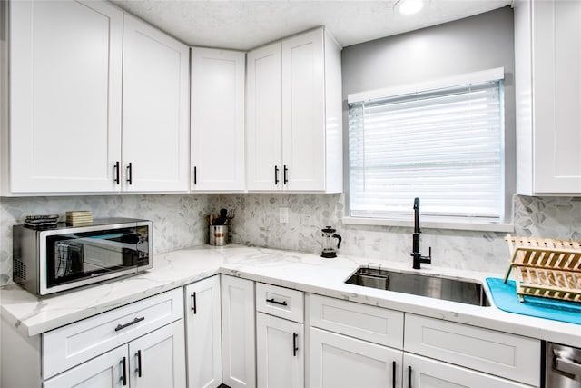 kitchen featuring appliances with stainless steel finishes, white cabinetry, a sink, and tasteful backsplash