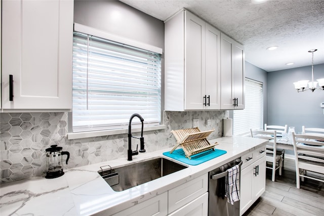 kitchen with light stone counters, a notable chandelier, a sink, white cabinets, and decorative light fixtures