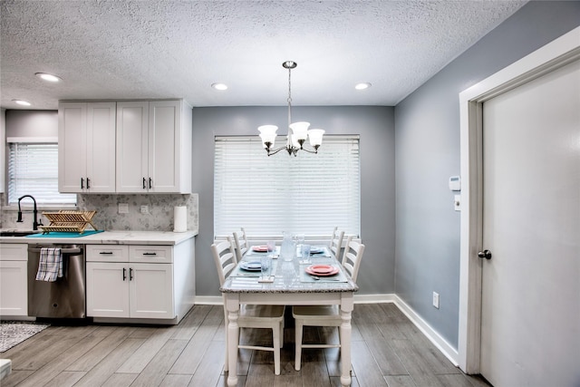 kitchen with stainless steel dishwasher, light wood-type flooring, decorative light fixtures, and white cabinets