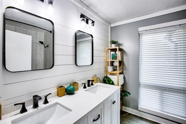 bathroom featuring double vanity, a textured ceiling, walk in shower, and a sink