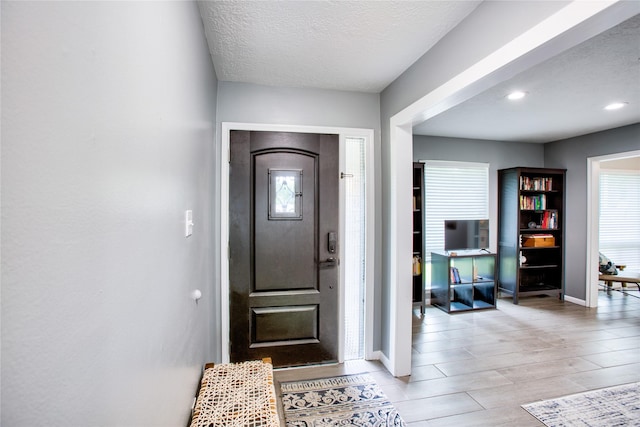 foyer featuring light wood-type flooring, plenty of natural light, baseboards, and a textured ceiling