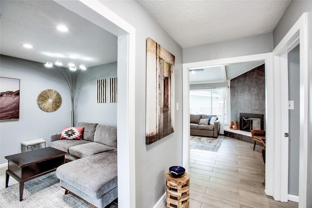 living area with a textured ceiling, a tile fireplace, light wood-style flooring, and baseboards