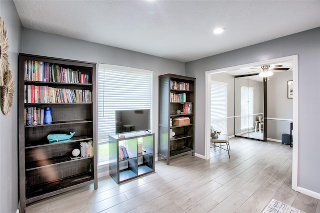 interior space with baseboards, ceiling fan, light wood-type flooring, and a healthy amount of sunlight