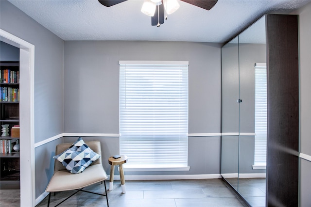 living area with a healthy amount of sunlight, ceiling fan, a textured ceiling, and baseboards