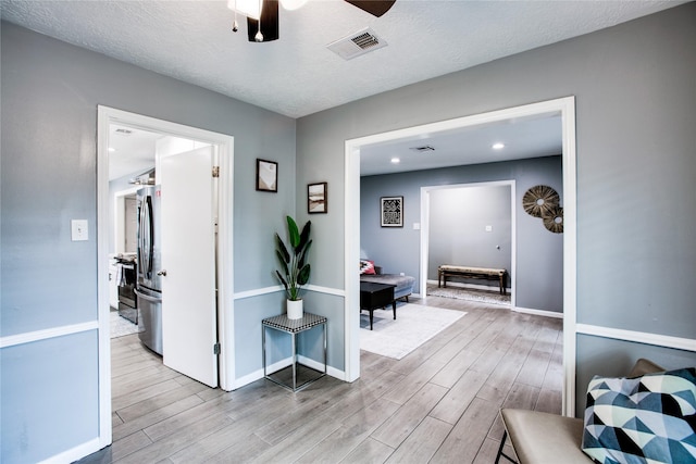 hall featuring a textured ceiling, light wood finished floors, and visible vents