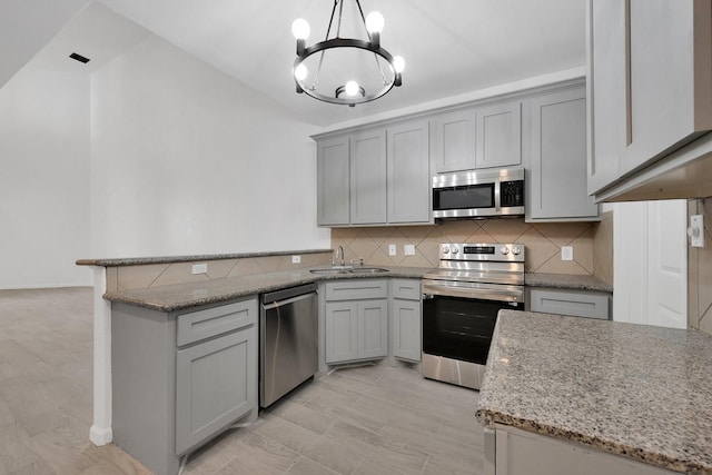 kitchen featuring hanging light fixtures, light stone countertops, a sink, stainless steel appliances, and backsplash