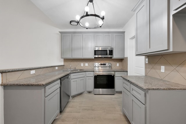 kitchen featuring light stone counters, a sink, appliances with stainless steel finishes, gray cabinets, and decorative light fixtures