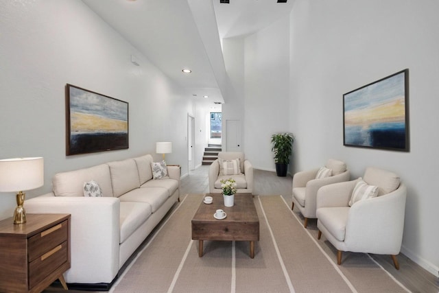 living area featuring recessed lighting, a high ceiling, baseboards, stairs, and light wood finished floors