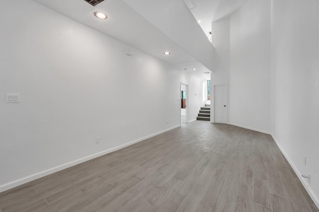 unfurnished room with light wood finished floors, baseboards, a towering ceiling, stairs, and recessed lighting